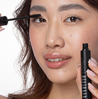 En kvinne blir sett påføre mascara på øynene, mens hun holder penselen forsiktig mens hun forsterker vippene.