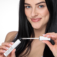 En kvinne holder elegant en tube med Nanolash-mascara, og viser sin skjønnhet og selvtillit i en stilig setting.