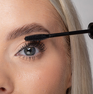 En kvinne bruker en mascarabørste for å påføre mascara, og forbedrer øyevippene på en dyktig måte for et mer dramatisk utseende.