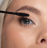 En kvinne påfører forsiktig mascara på øyevippene med en mascarabørste, og forbedrer øyesminken med presisjon.