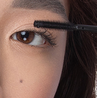 En kvinne blir sett påføre mascara med en børste, med fokus på øyevippene for å oppnå et definert og elegant utseende.